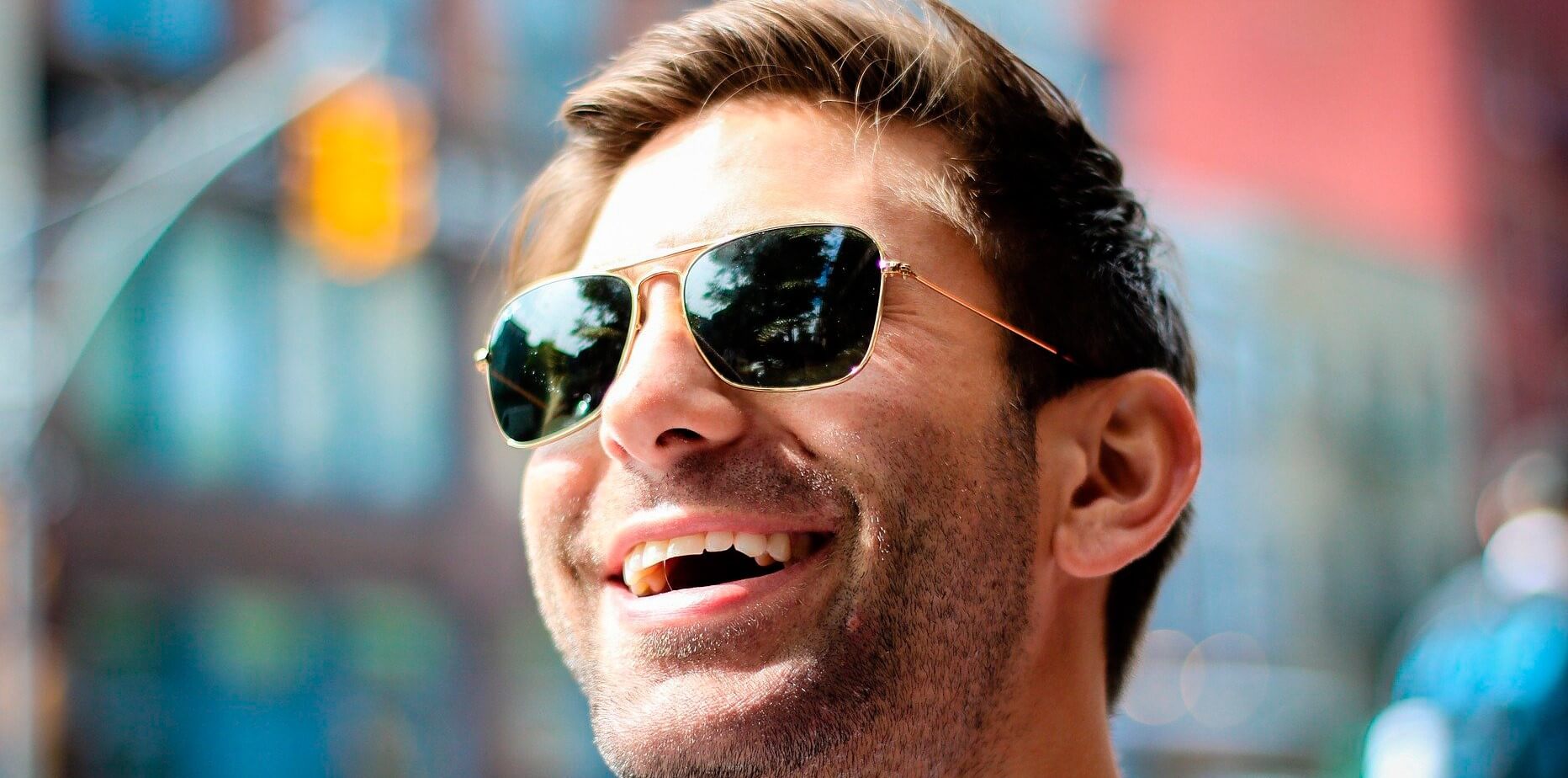 hombre feliz con gafas de sol sonríe en la ciudad